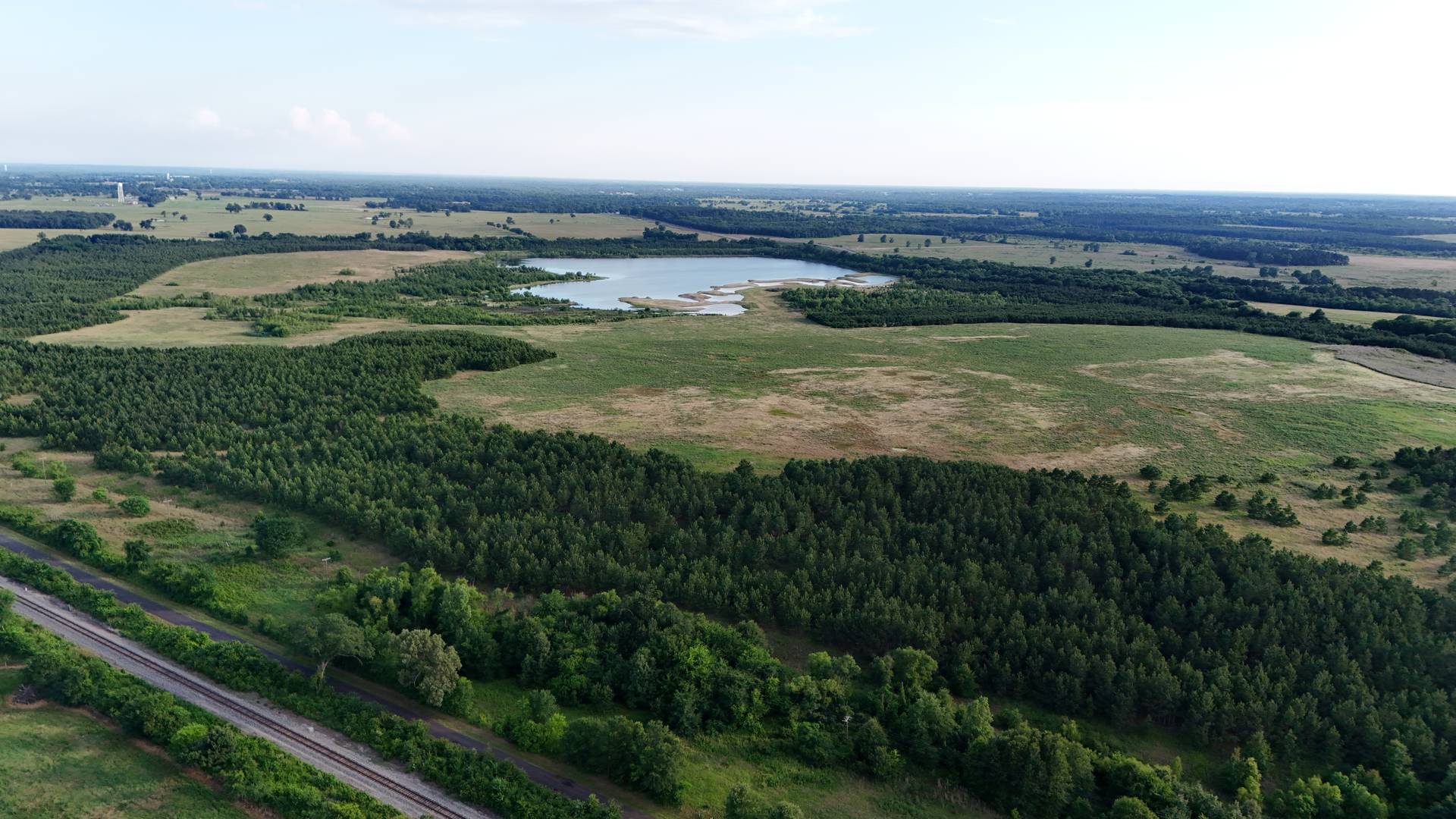 Aerial view over East Texas acreage at golden hour: open pasture, tree lines and a lake.